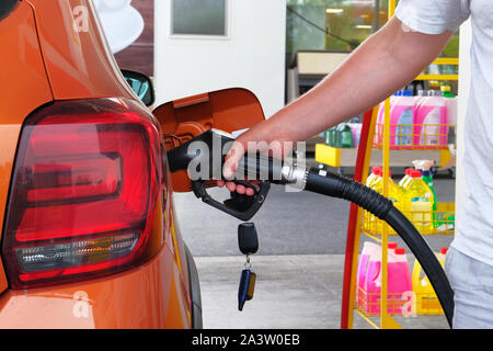 Pumpen Benzin in orange Auto an einer Tankstelle. Zu Auto mit Kraftstoff in Tankstelle füllen. Tankstelle Pumpe. Close Up. Stockfoto