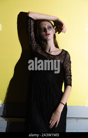 Ernsthafte junge Frau mit Halloween Make-up auf gelben Hintergrund mit Schatten Stockfoto