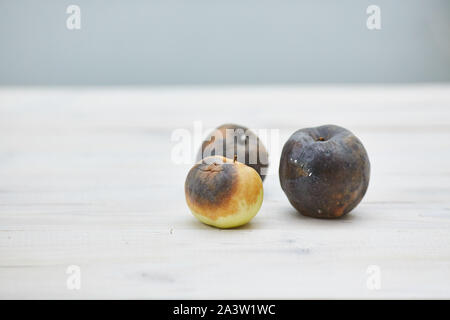 Hässlich Obst. Drei faulen Äpfeln auf dem hölzernen Tisch Stockfoto