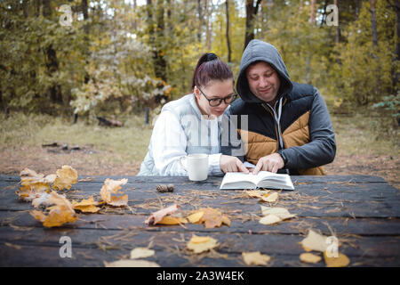 Stattliche Liebespaar auf der Bank im Herbst Park mit einem Buch sitzen, gemeinsam Spaß zu haben. Liebe und Zärtlichkeit. Beziehungen, Freundschaften Stockfoto
