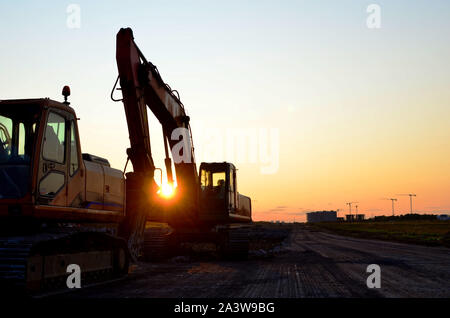 Große Raupenbagger mit mit hydraulischer Hammer bricht Asphalt auf einer Baustelle auf dem Hintergrund Sonnenuntergang. Road Repair, Asphalt replac Stockfoto