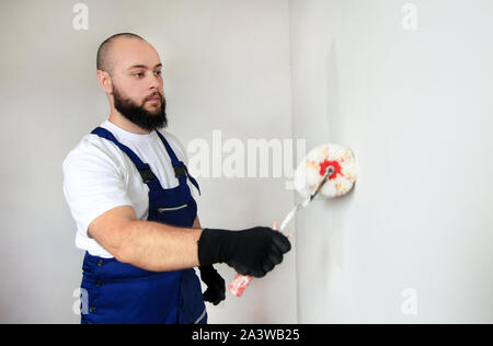 Bauarbeiter tun beenden Renovierung im Apartment. Professionelle Maler Auftragnehmer mit weißer Farbe bürstenrolle Malerei der Betonwand. Stockfoto