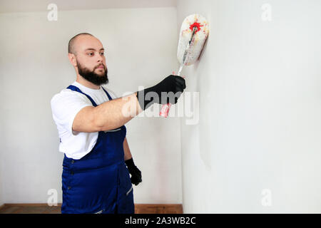 Bauarbeiter tun beenden Renovierung im Apartment. Professionelle Maler Auftragnehmer mit weißer Farbe bürstenrolle Malerei der Betonwand. Stockfoto