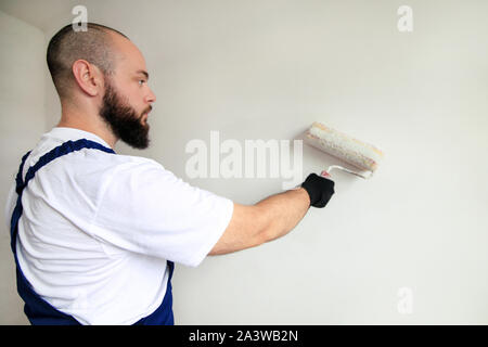 Bauarbeiter tun beenden Renovierung im Apartment. Professionelle Maler Auftragnehmer mit weißer Farbe bürstenrolle Malerei der Betonwand. Stockfoto