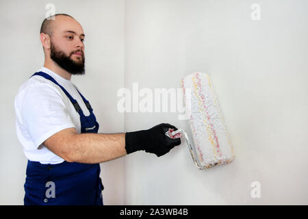 Bauarbeiter tun beenden Renovierung im Apartment. Professionelle Maler Auftragnehmer mit weißer Farbe bürstenrolle Malerei der Betonwand. Stockfoto