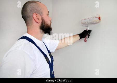 Bauarbeiter tun beenden Renovierung im Apartment. Professionelle Maler Auftragnehmer mit weißer Farbe bürstenrolle Malerei der Betonwand. Stockfoto