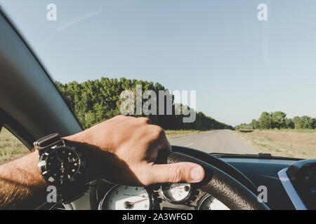 Eines Mannes Hand mit mit einem Smart watch auf das Lenken der Räder eines Autos während der Fahrt auf der Autobahn. Ein Mann fährt auf der Straße außerhalb der Stadt. Stockfoto