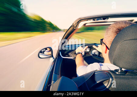 Mann fahren ein Cabrio Auto auf Landstraße. Blick von innen hinter dem Fahrer. der mensch ist das Fahren mit hoher Geschwindigkeit auf der Autobahn. Gefährlich schnell dri Stockfoto