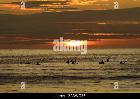 Surfer silhouetted gegen die untergehende Sonne, wie Sie für die nächste grosse Wellen an Barvas Bay warten, auf der atlantischen Küste der Insel Lewis, Schottland. Stockfoto