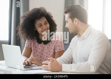 Multirassische Gesellschaft Mitglieder am Schreibtisch sitzen, reden und lächeln Stockfoto