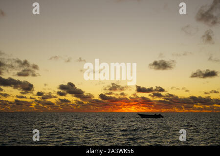 Ein Ruderboot ist bei Sonnenuntergang in einer Lagune in der Nähe der Insel Fakarava in Französisch Polynesien im Südpazifik verankert Stockfoto