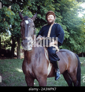 Der deutsche Bass Sänger Ivan Rebroff in traditioneller russischer Kleidung auf einem Pferd, Deutschland München Anfang 1980er. Stockfoto