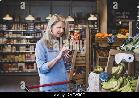 Ältere Frauen tun, wöchentliche Lebensmittelgeschäft mit Smartphone Stockfoto
