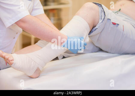 Krankenschwester Bandagen das Bein. Bruch der unteren Gliedmaßen. Behandlung von gebrochenen Knochen. Ein Gips verhängen. Patienten der chirurgischen Abteilung. Der Arzt die Hände Stockfoto