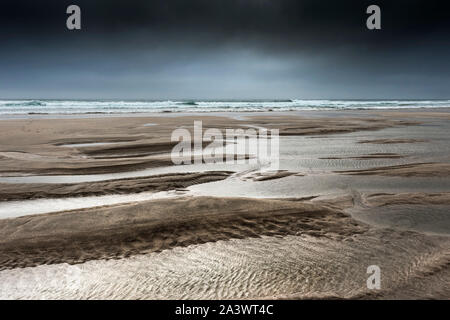 Ebbe als dunkle, dramatische Wolken auf den Fistral Beach in Newquay in Cornwall. Stockfoto