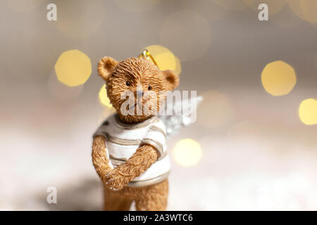 Dekorative Figuren aus einem Thema Weihnachten. Figurine eines süßen Bär mit Angel Wings. Festliches Dekor, warme Bokeh leuchtet. Stockfoto