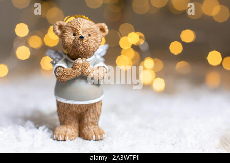 Dekorative Figuren aus einem Thema Weihnachten. Figurine eines süßen Bär mit Angel Wings. Festliches Dekor, warme Bokeh leuchtet. Stockfoto