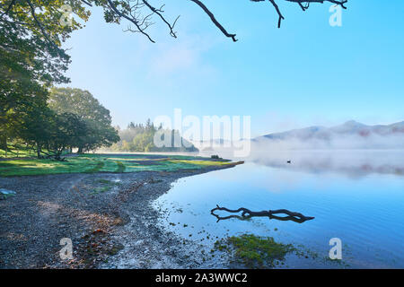 Dawn Cloud beginnt, scheint die Sonne durch den Nebel über einem Waldgebiet am See Derwentwater abzuführen, Lake District, Cumbria, England. Stockfoto