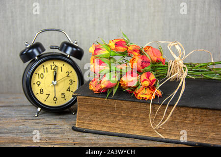 Orange Rose Bouquet auf alten Buch mit retro Wecker Stockfoto