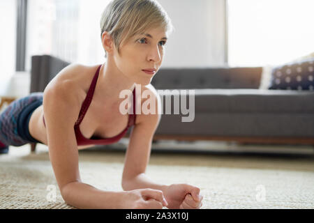 Tausendjährige gesunde Mädchen mit kurzen Haaren, inproving ihr Core Stärke und Stabilität durch Halten Plank in Ihrem Wohnzimmer Stockfoto