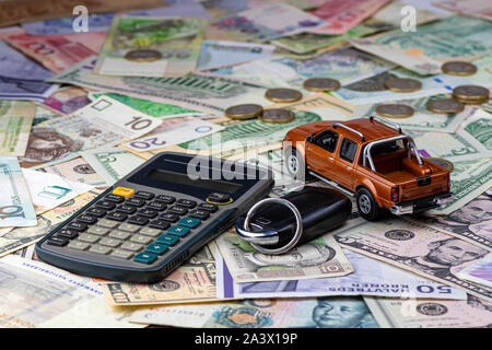 Taschenrechner, Tasten und Pickup Spielzeugauto auf eine Vielzahl von nationalen Banknoten Hintergrund. Die Kosten für die Anschaffung, Miete und maintainin Stockfoto