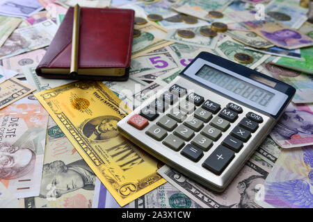 Taschenrechner, Notizbuch und Bleistift auf dem Hintergrund der unterschiedlichen Land Währung Noten und ein symbolisches Gold Dollar Banknote. Finanzielle Planung conce Stockfoto