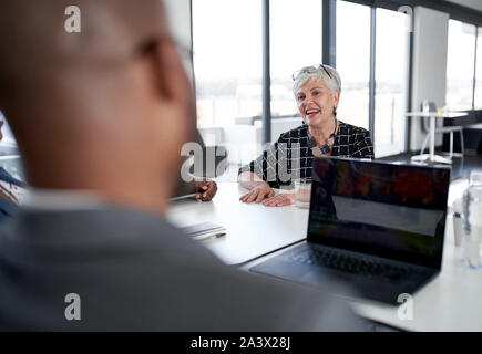 Unposed Schuß des Bevollmächtigen der Schönen senior Geschäftsfrau lächelnd mit afrikanischen amerikanischen Geschäftsleuten in großen modernen Office Conference rooom mit Ta Stockfoto