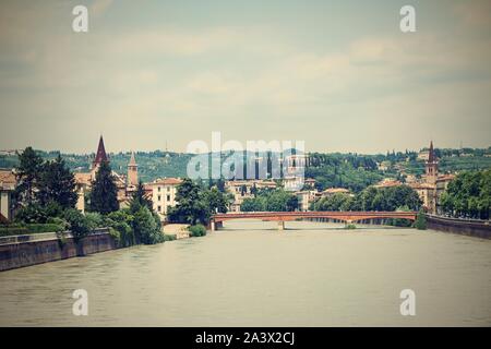 Horizontale Foto mit Blick auf die Etsch. River fließt durch die berühmten Stadt Verona in Italien. Alte Brücke und mehrere Gebäude sind im Hintergrund sichtbar Stockfoto