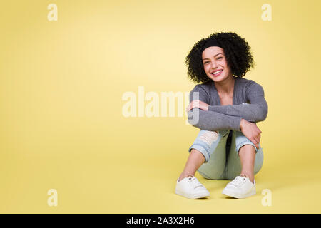 Glückliches Mädchen sitzt lächelnd auf gelbem Hintergrund mit kopieren. Stockfoto