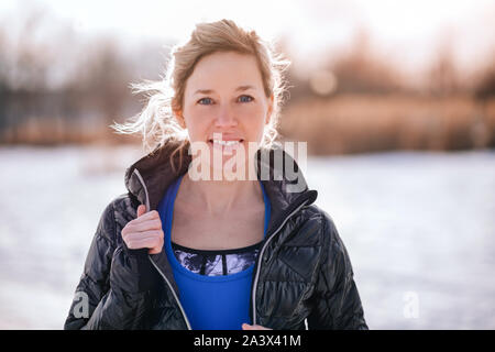 Porträt eines sportlichen blonde Frau fit halten einen kalten Wintertag durch Spazieren gehen, in eine verschneite Stadt Stockfoto