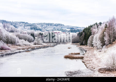 Ein Fluß, der durch ein norwegisches Dorf im Winter schneebedeckten Tag im Skedsmo, eine Gemeinde in der Grafschaft Akershus, Norwegen vorbei. Stockfoto