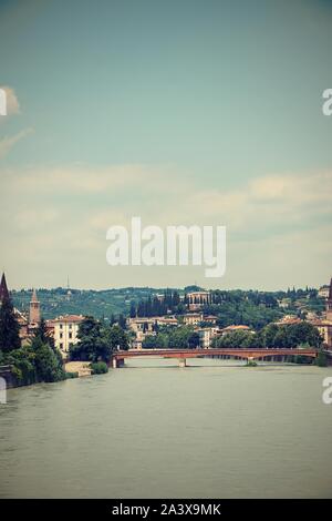 Vertikale Foto mit Blick auf die Etsch. River fließt durch die berühmten Stadt Verona in Italien. Alte Brücke und mehrere Gebäude im Hintergrund sichtbar. Stockfoto