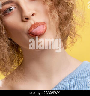 Nahaufnahme der jungen Frau an der Kamera auf der Suche und zeigt die Zunge auf gelb isoliert Hintergrund. Kurzen Haaren curly Girl posiert und lächelnd im Studio. Konzept des Glücks und der Kinder. Stockfoto