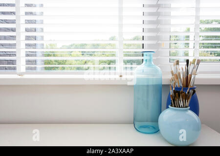 Pinsel auf einem weißen Holztisch, closeup Pinsel in modernen blau Vase in der Nähe der Fenster, modernen hellen Innenraum Stockfoto