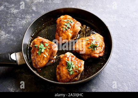 Süß und würzig Honig gegrillte Hähnchen Schenkel in der Pfanne auf dunklen Tisch aus Stein. Lecker essen im asiatischen Stil. Stockfoto