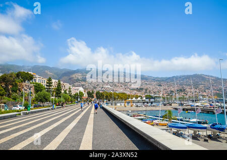 Funchal, Madeira, Portugal - 14.September 2019: Straßen in der Hauptstadt der portugiesischen Insel. Die Stadt auf dem Hügel im Hintergrund. Die Menschen auf der Straße, das tägliche Leben. Hafenpromenade. Hafen, Marina. Stockfoto