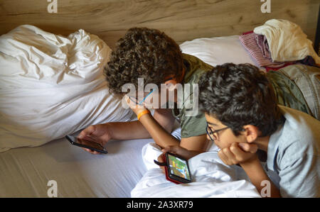 Frankfurt am Main, Deutschland, August 2019. Im Hotel A&o Zwei junge Gäste auf dem Doppelbett entspannen spielen mit Ihrem Smartphone. Stockfoto