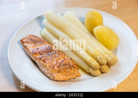 Weißer Spargel, Spargelspitzen, gekocht, mit Kartoffeln und ein gebratenes Lachsfilet, auf Platte, mit flüssiger Butter, Stockfoto