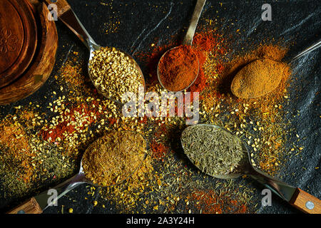 Verschiedene Gewürze auf einem schwarzen Stein. Orientalische Gewürze in Löffel, Paprika, Curry, Kräutern auf schwarz metallic Fach im asiatischen Stil. Flach, zu Stockfoto
