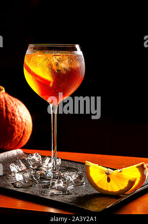 Aperol Spritz Cocktail mit Kürbis, Orangenscheiben und Eiswürfel auf Black metal Fach auf dunklem Hintergrund. Halloween und Herbst Konzept für Party, Event Stockfoto