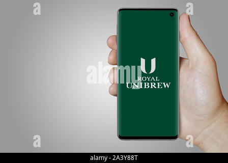 Ein Mann hält ein Telefon mit dem Logo des Unternehmens Royal UNIBREW aufgeführt im OMX Kopenhagen. Grauen Farbverlauf Hintergrund. Credit: PIXDUCE Stockfoto