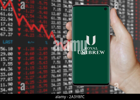 Ein Mann hält ein Telefon mit dem Logo des Unternehmens Royal UNIBREW aufgeführt im OMX Kopenhagen. Negative Börse. Credit: PIXDUCE Stockfoto