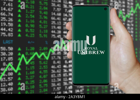 Ein Mann hält ein Telefon mit dem Logo des Unternehmens Royal UNIBREW aufgeführt im OMX Kopenhagen. Positive Börse. Credit: PIXDUCE Stockfoto