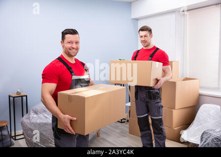 Portrait von zwei lächelnde Junge männliche Umzug Arbeiter, die Kartons im Wohnzimmer Stockfoto