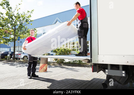 Junge männliche Movers Entladen der gewickelte Matratze aus fahrenden Fahrzeugs Stockfoto