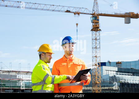 Männliche Architekten erteilen Anweisungen an seine Vorarbeiter auf Zwischenablage Arbeiten auf der Baustelle Stockfoto