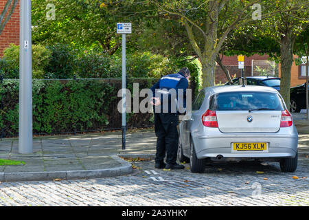 Ein verkehrspolizist Ausstellung ein Parkticket auf einem geparkten Auto Stockfoto