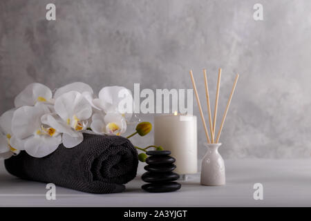 Spa Massage und Wellness Handtuch aroma Sticks schwarze Steine Kerze und Orchideen auf grauem Stein Background Copy space Stockfoto