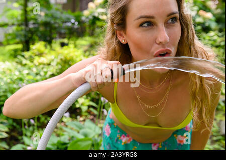 Junge Frau trinkt aus Gartenschlauch Stockfoto