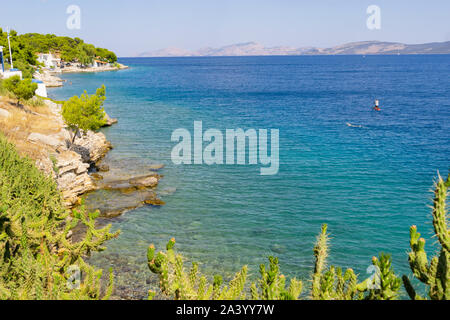 Ermioni, Griechenland - 20 Juli 2019; Paddleboarder und Schwimmer Position entlang der felsigen Mittelmeerküste. 1 Stockfoto